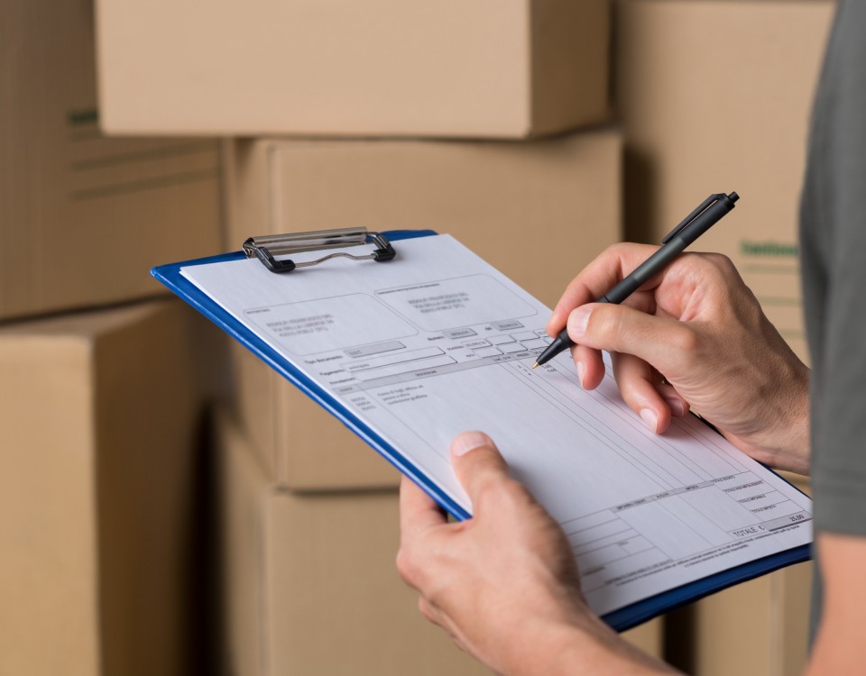 Warehouse manager signing dispatch sheet. Close up hand of manager checking delivery order. Young freight manager checking invoice with cardboard box parcel.